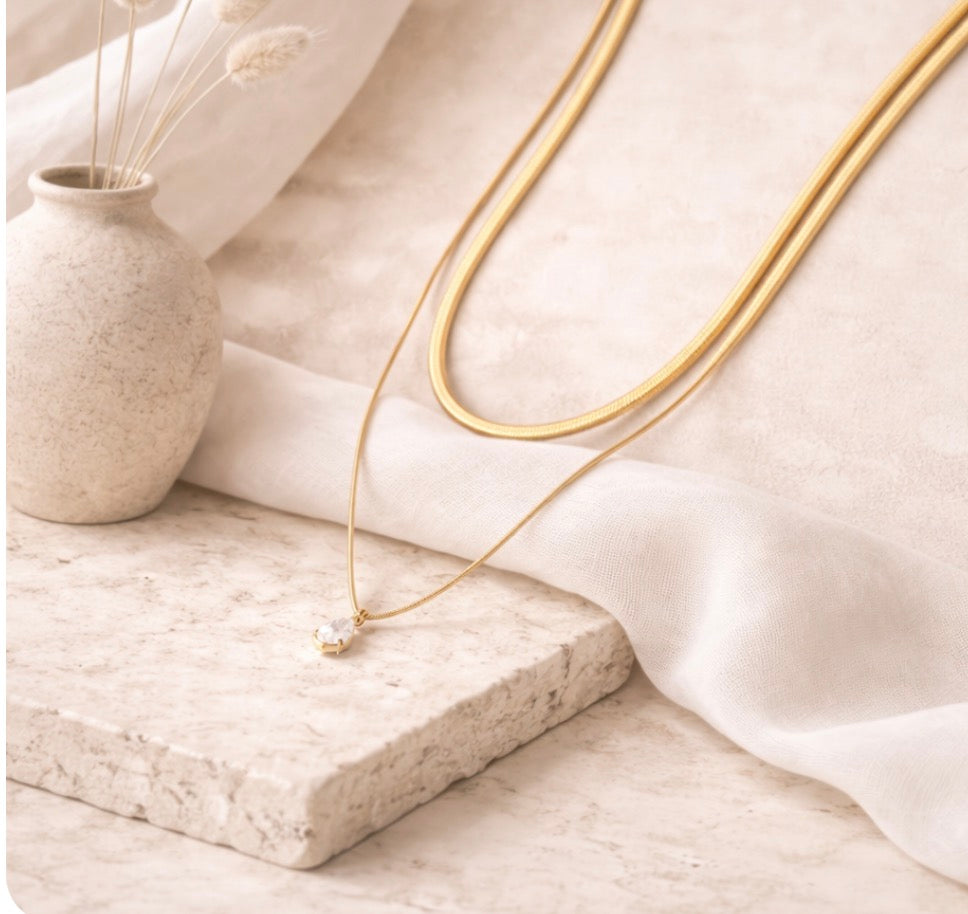Delicate gold-toned necklace from the Silver Collection featuring a small crystal pendant, styled with soft natural elements in a serene setting.
