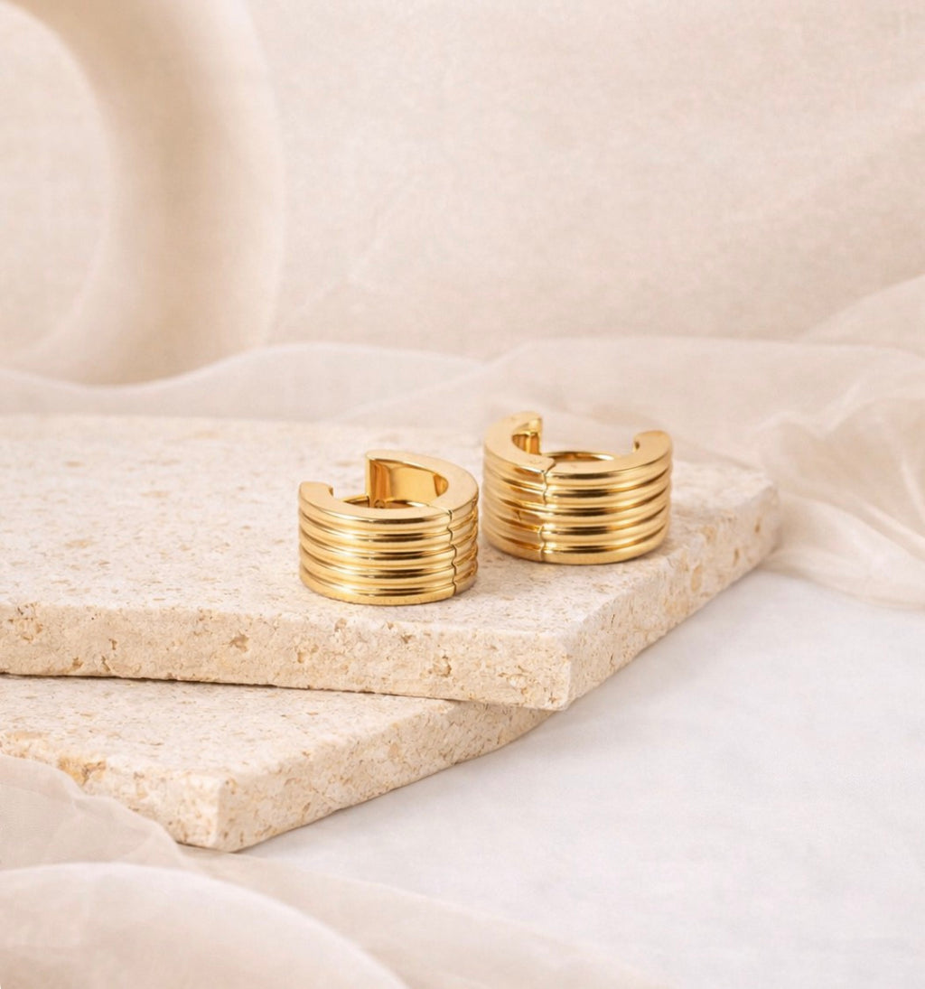 Pair of 18K gold plated ribbed hoop earrings resting on textured stone slabs, showcasing waterproof and tarnish resistant jewelry from the Earrings collection.