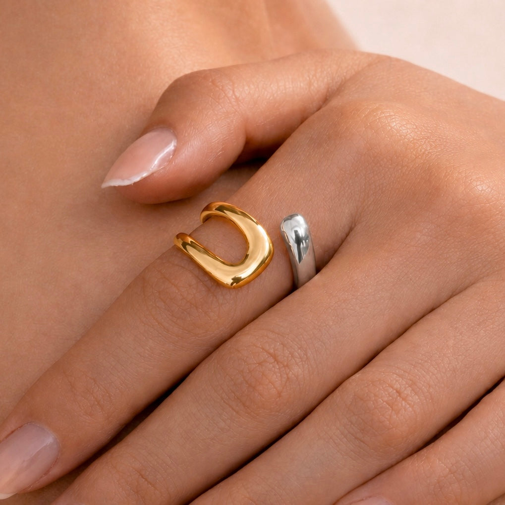 Close-up of a hand wearing two rings from the Silver Collection, featuring a polished gold-tone open ring alongside a sleek silver band, showcasing modern and elegant styling.