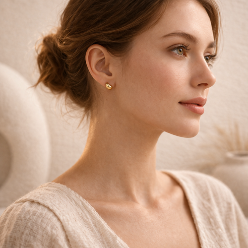 Close-up of a woman wearing elegant, small gold pebble-shaped earrings from the Earrings collection, highlighting a minimal and modern look suitable for everyday wear.