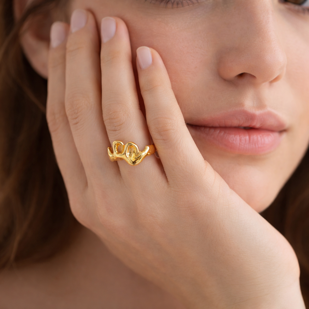 Close-up of a woman's hand wearing a gold wave sculpture ring, showcasing its unique, fluid design from the Rings collection, ideal for stylish, waterproof jewelry lovers.