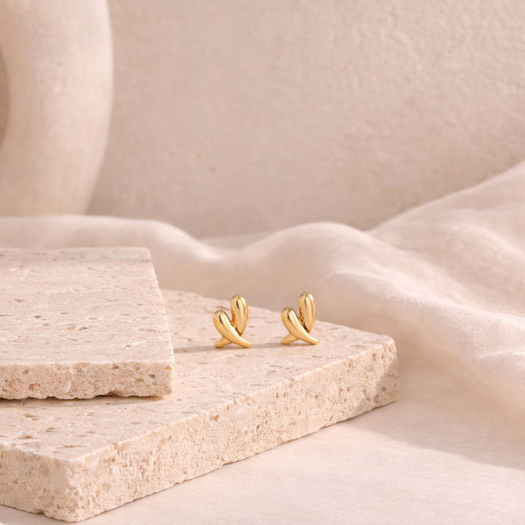 Pair of elegant gold-tone heart-shaped earrings displayed on textured stone slabs, showcasing delicate craftsmanship from the Earrings collection, ideal for everyday wear.