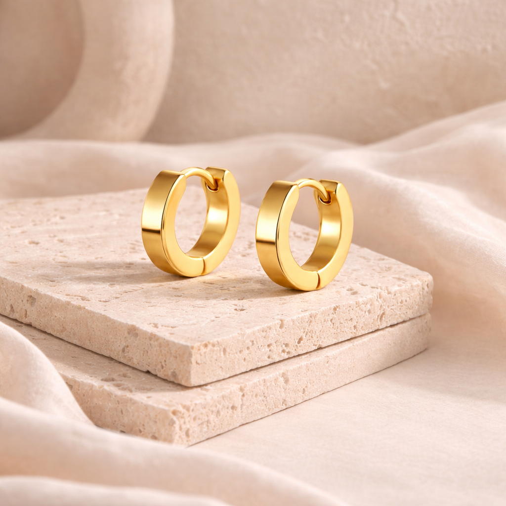 Pair of sleek gold-colored huggie earrings displayed on textured stone slabs, highlighting a modern, minimalist design perfect for the Earrings collection.