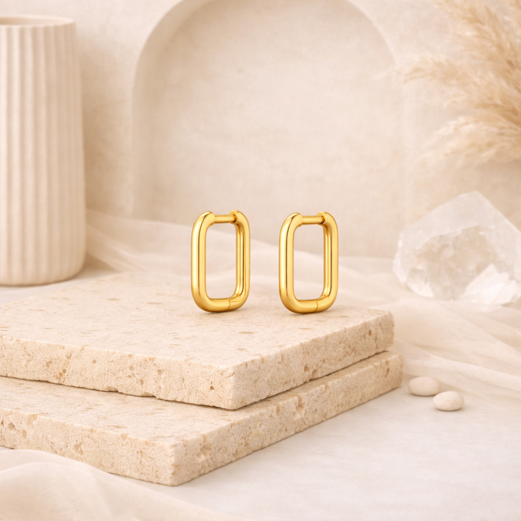 Pair of polished gold-tone rectangular hoop earrings displayed on textured stone slabs with neutral beige and cream decor, part of elegant waterproof earrings collection.