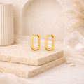 Pair of polished gold-tone rectangular hoop earrings displayed on textured stone slabs with neutral beige and cream decor, part of elegant waterproof earrings collection.