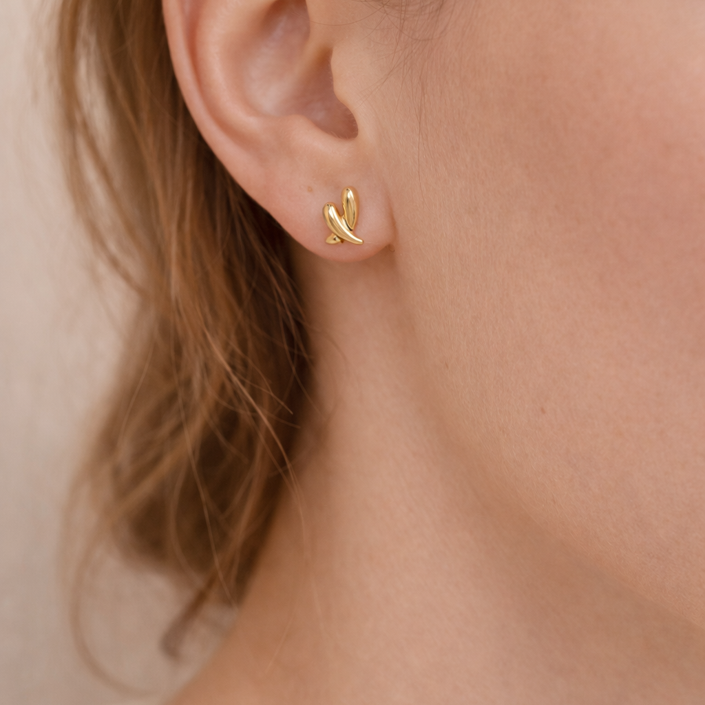 Close-up of a delicate, gold-toned heart-shaped earring worn on the ear, showcasing elegant minimalistic design from the Earrings collection.