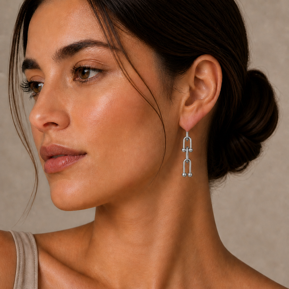 Close-up of a woman wearing silver drop earrings with a modern linked design, styled with natural makeup and hair in a low bun, featured in the Silver Collection earrings.
