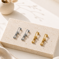 Two pairs of Luna Link Drop Earrings in silver and gold tones displayed on a textured stone block, highlighting elegant, modern designs from the Silver Collection and Earrings category.