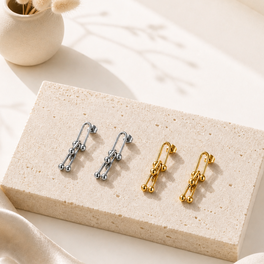 Two pairs of Luna Link Drop Earrings in silver and gold tones displayed on a textured stone block, highlighting elegant, modern designs from the Silver Collection and Earrings category.