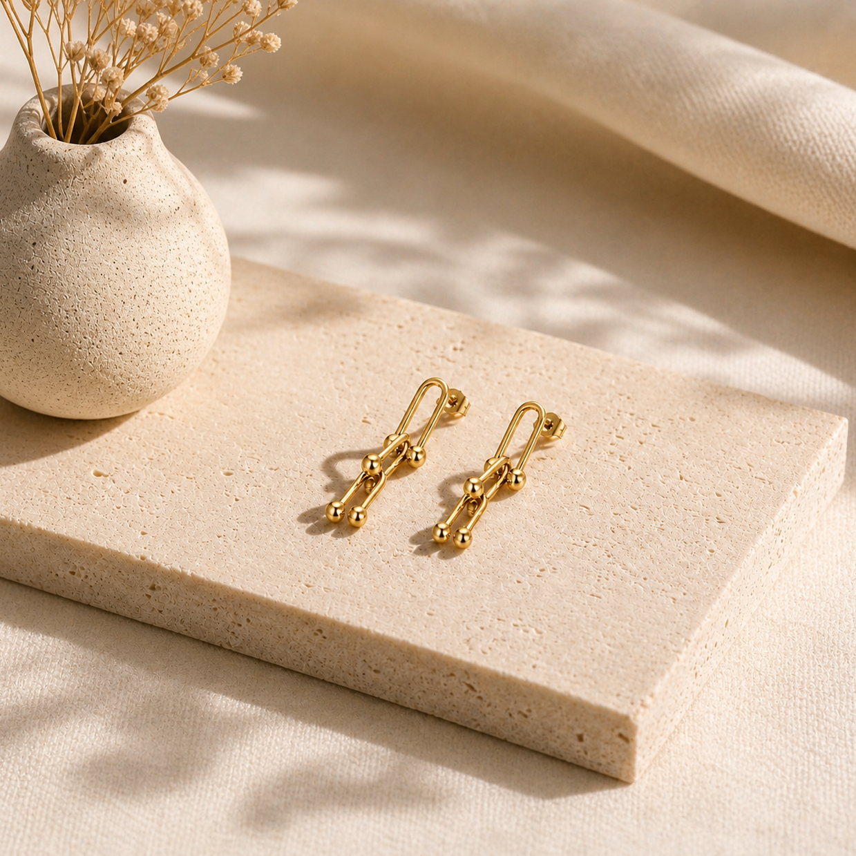 Delicate gold-tone drop earrings displayed on a textured stone slab, styled with neutral dried florals, part of the Silver Collection and waterproof jewelry shop.