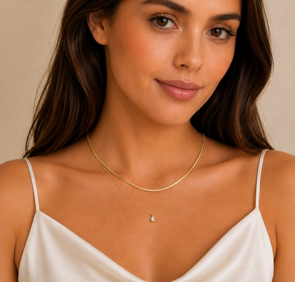 Close-up of a woman wearing two delicate gold necklaces from the Silver Collection, featuring a subtle raindrop crystal pendant and sleek layering perfect for everyday elegance.
