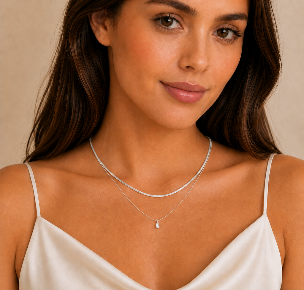 Close-up of a woman wearing a delicate silver necklace with a small crystal snake pendant from the Silver Collection, styled with a satin off-white top.