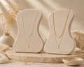 Two elegant layered necklaces displayed on beige velvet stands, one silver and one gold-toned, featuring delicate raindrop crystal pendants from the Silver Collection in a minimalistic setting.